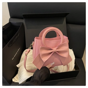 Pink crossbody bag detail featuring a large bow and gold hardware in a gift box