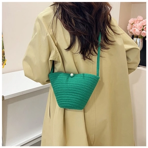 Close-up of green hand-woven bucket bag with pearl button on a beige trench coat