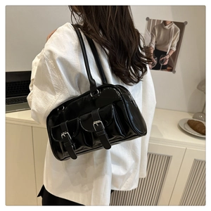Detail of glossy black underarm bag with silver buckles in a minimalist studio setting