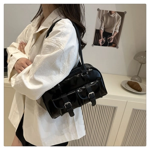 Detail of black glossy patent leather shoulder bag with double front buckle pockets