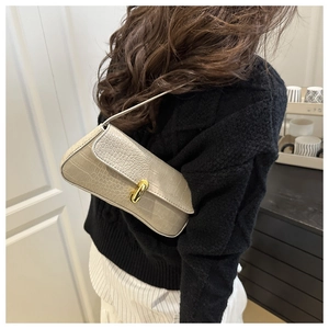 Detail view of beige crocodile embossed leather bag with gold buckle on shoulder