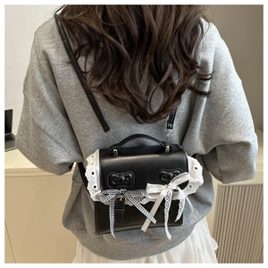 Close-up of black leather crossbody bag with delicate white lace trim and bow details