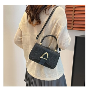 Detailed view of a black glitter crossbody bag with a gold triangular buckle on a model
