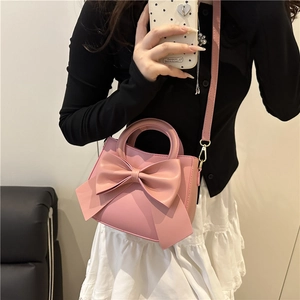 Pink crossbody square bag with a large bow and gold hardware shown on a model