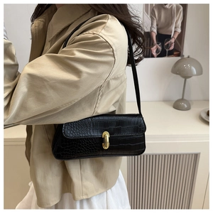 Detail of black faux crocodile leather baguette bag with a stylish gold oval metal lock