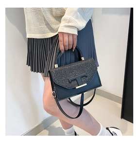 Detail of a chic black crossbody bag featuring a glittery flap and metal T-shaped logo