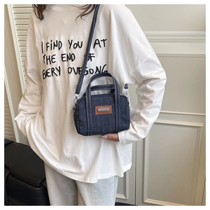 Detail of dark blue denim crossbody bag with contrast stitching and brown leather patch