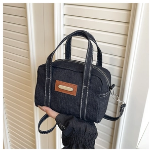 Detail of black denim crossbody bag with contrast stitching and leather patch