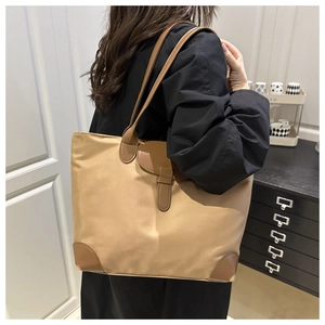 Detail view of khaki nylon tote bag with brown leather handles worn by a model