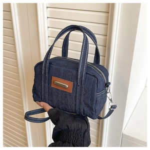 Detail of a dark blue denim crossbody bag featuring white contrast stitching and leather patch