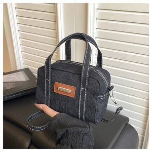 Detail of dark blue denim tote bag with white stitching and leather patch on dark surface