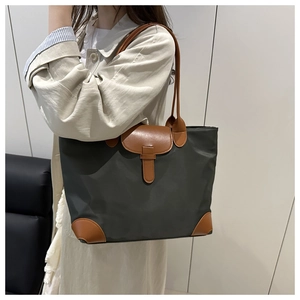 Detail of grey nylon tote bag with brown leather handles worn by a model