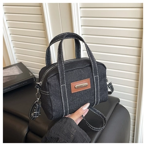 Detail of black denim crossbody bag with contrast white stitching and leather patch decoration