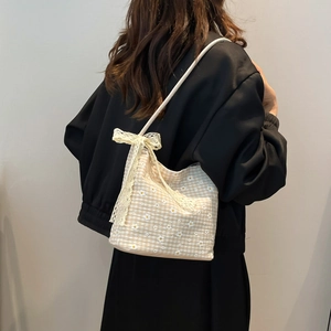 Sac seau beige à carreaux avec broderies marguerites et nœud en dentelle, porté épaule