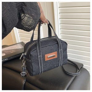 Detail of blue denim crossbody bag featuring white contrast stitching and silver hardware