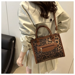 Close-up of leopard print tote bag with brown leather handles worn by model in trench coat