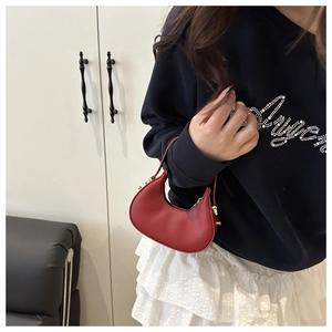 Detail view of a luxury red leather mini dumpling bag with gold zipper held by a model