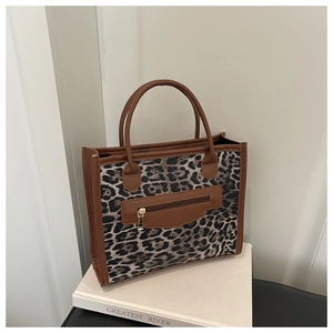 Detail of leopard print tote bag featuring brown leather trim and front zipper pocket