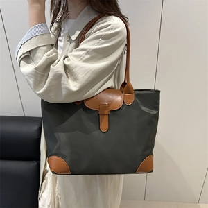 Minimalist deep green nylon tote bag with brown leather handles in a modern indoor setting