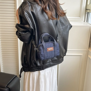 Retro navy denim crossbody bag with brown leather patch and white stitching on a model