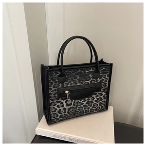 Detail of grey leopard print tote bag with black handles and metal zipper on white book