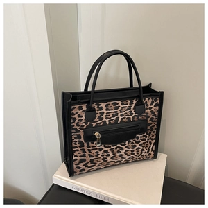 Detail of leopard print tote bag featuring black leather handles and zipper pocket