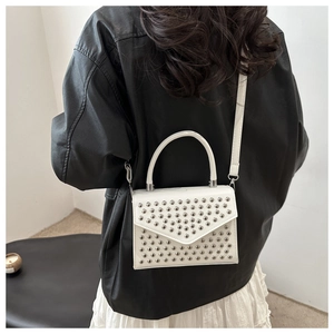Detail of white PU leather crossbody bag with silver dome studs shown on model
