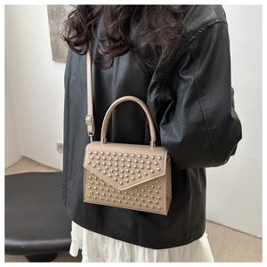 Detail of studded apricot PU leather crossbody bag worn over a black leather jacket