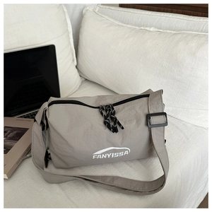 Detailed view of light grey nylon messenger bag with woven zipper pull on white bedding