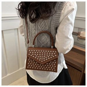 Detailed view of brown crossbody bag with silver studs worn by a model in casual setting