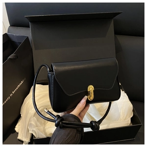 Détail d'un sac bandoulière noir avec boucle dorée et bandoulière nouée sur soie
