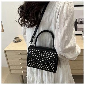 Detail of a black leather crossbody bag with silver studs worn by a model in a cozy setting