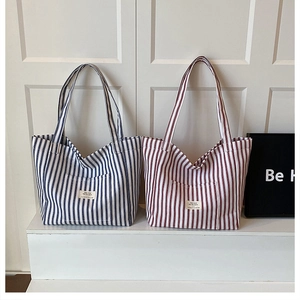 Detail of red and blue striped canvas tote bags with front pockets on a white stand