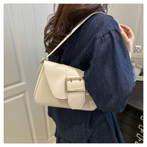Close-up of cream leather shoulder bag with a prominent gold buckle in a minimalist design