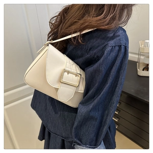 Detail of minimalist cream leather shoulder bag with bold gold square buckle on model