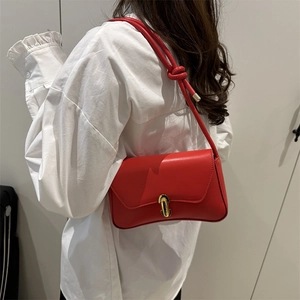 Sac bandoulière rouge en cuir avec fermoir pilule doré sur fond de chemise blanche