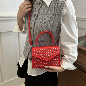 Women's red leather crossbody bag with silver studs and top handle on a fashion model