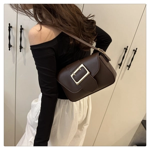 Detail of dark brown leather crossbody bag with large gold buckle worn on shoulder