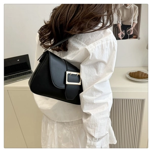 Detail of a black leather shoulder bag with a large gold square buckle on a model