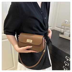 Détail d'un sac bandoulière en cuir marron avec fermoir doré texturé et bandoulière chaîne