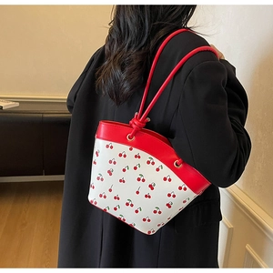 Detail view of cherry print shoulder bag with red knotted leather handle on model