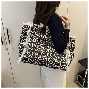 Detail of large leopard print tote bag with white tassel trim and black shoulder straps