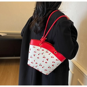 Detail of red and white cherry print bucket bag with knotted leather strap on model