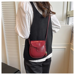 Détail du sac selle en cuir verni bordeaux avec breloque fraise et logo rond