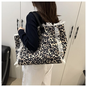 Fashionable leopard print tote bag with white tassel fringe accents shown on shoulder