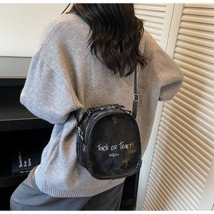 Detail of a black leather crossbody bag featuring unique white cursive script printing