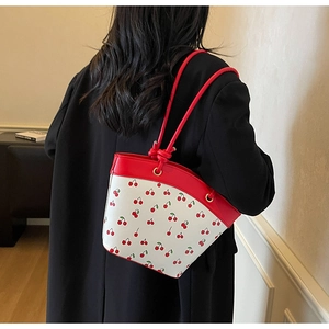 Detail of red cherry print bucket bag with knotted handle shown on model shoulder