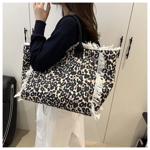 Detail of leopard print tote bag featuring white fringe edges and black round handles