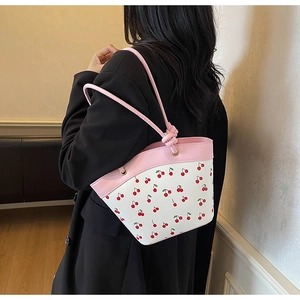Detail showing white cherry print bucket bag with pink knotted handle on a model shoulder