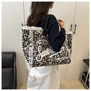 Close-up of leopard print tote bag featuring white fringe edges and artistic lettering